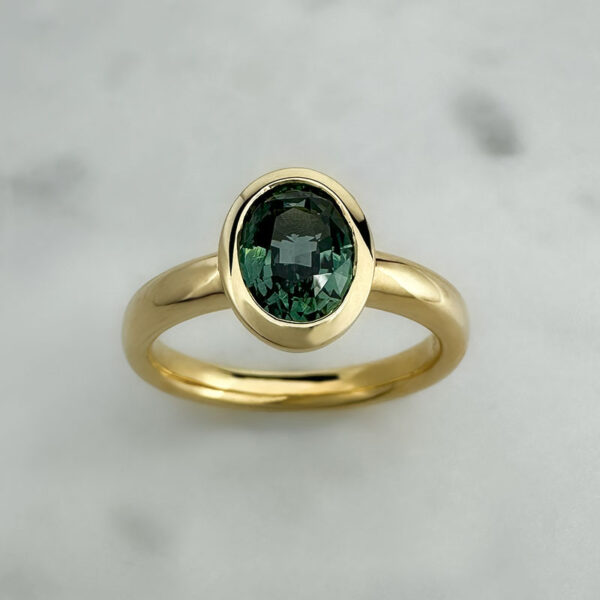 Teal sapphire in a yellow gold bezel set solitaire ring