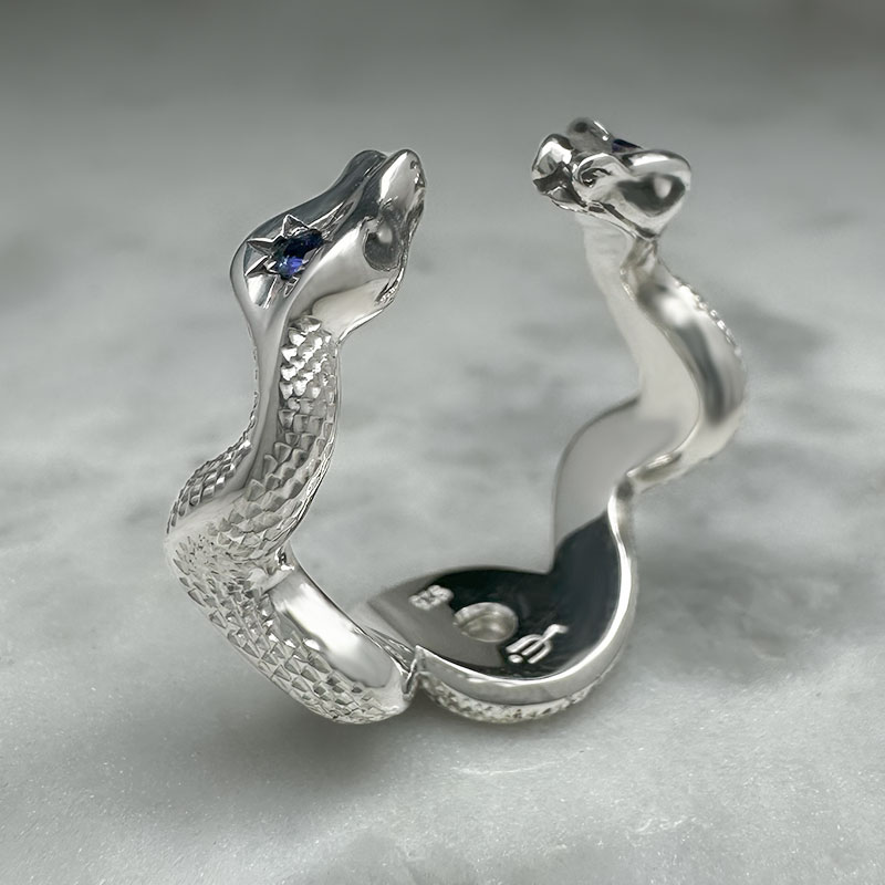 silver ring with two entwined snakes with engraved scales and sapphires set into their heads